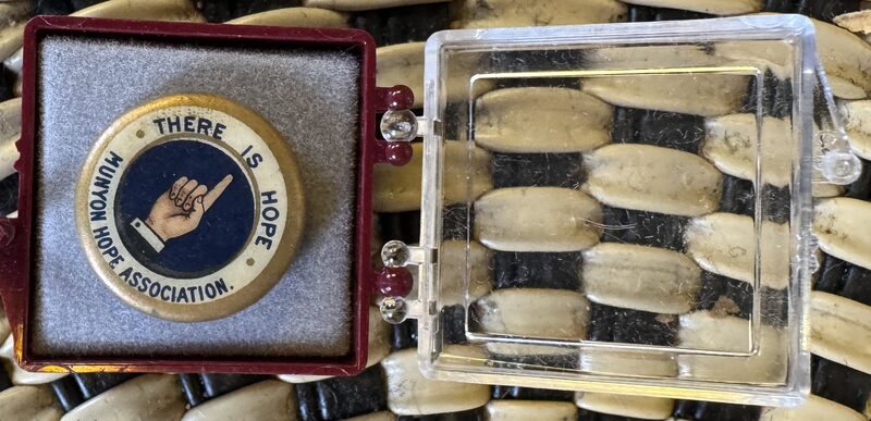 A round pin with a blue center showing an illustration of a pointing hand and the text 'THERE IS HOPE' and 'Munyon Hope Association'.
