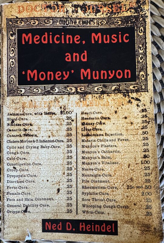 A stained, weathered book cover with an ornate border and a central black panel reading 'Medicine, Music and 'Money' Munyon' in red type, surrounded by a two-column list of old-fashioned 'cures' and prices. The bottom features a red-black label with the author name 'Ned D. Heindel.'